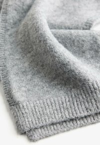 Grå uldstof hænger blødt og fremviser en tekstureret overflade med en ribbet kant. Materialet er varmt og indbydende, ideelt til koldt vejr.