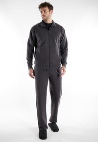 Chaqueta gris con cremallera y cuello blanco en contraste, pantalones grises a juego y zapatillas oscuras. Textura de tela suave, corte relajado y detalles mínimos.