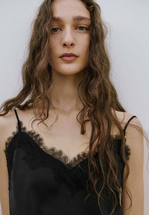 Camisole en satin noir avec une bordure en dentelle le long de l'encolure et des bretelles. Présente une texture lisse et une coupe décontractée.