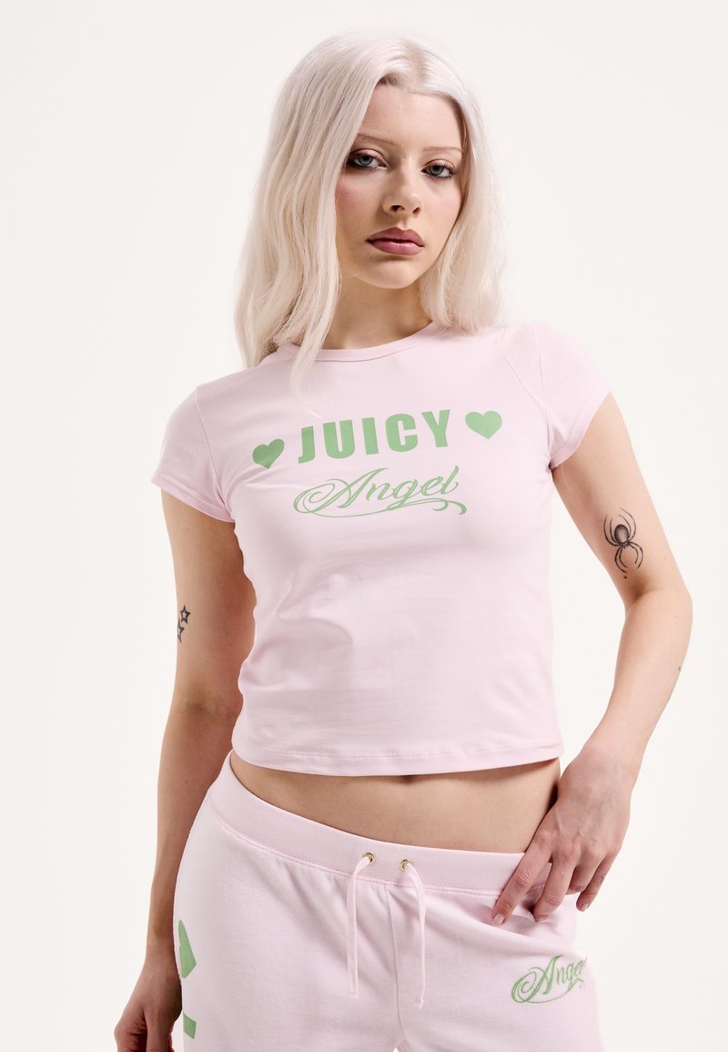 Rózsaszín rövid ujjú, rövidített póló zöld "JUICY" felirattal és szív motívumokkal. Puha anyagból készült, testhez simuló szabással, látható logó részlettel.