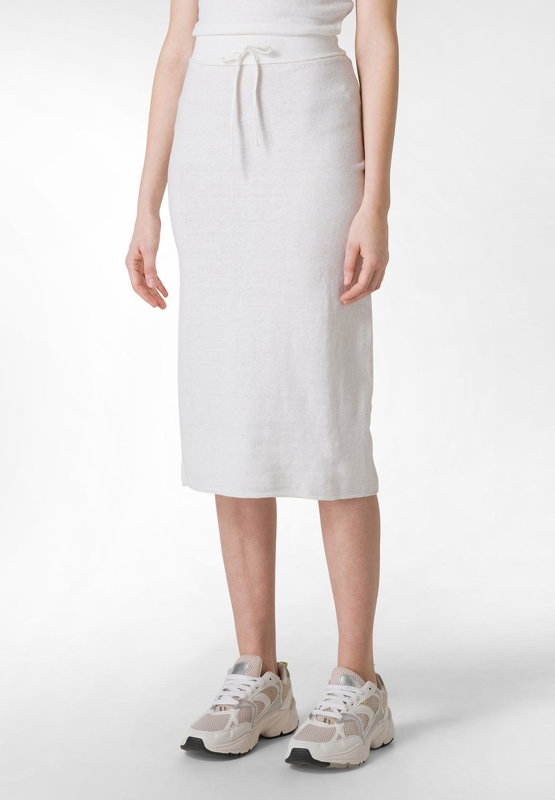 Falda midi de punto blanca con cintura ajustable, forma recta y tejido texturizado. Se lleva con zapatillas deportivas de color claro.