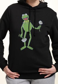 Haut à capuche noir avec un graphisme de Kermit la grenouille vert et des marguerites, présentant un design décontracté, des cordons de serrage et une texture douce.