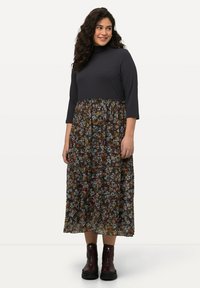 Czarna ribbed bluzka z wysokim dekoltem i rękawami 3/4, połączona z długą spódnicą w kwiecisty wzór w różnych kolorach. Uzupełniona botkami za kostkę.