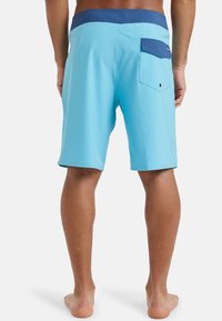 Shorts de bain bleu clair avec un waistband bleu foncé. Présente une poche arrière avec un rabat et un détail de bouton unique. Texture lisse.