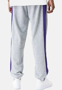 Pantaloni sportivi grigi con una finitura testurizzata, caratterizzati da strisce laterali viola uni e polsini elasticizzati. Indossati con sneaker bianche.