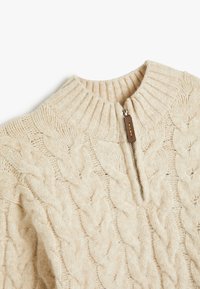 Cremfarbener Zip-Hals-Pullover mit einem Zopfmuster, ausgestattet mit einem gerippten Kragen und einem Leder-Zipper. Weicher Stoff mit dickem Strickdesign.