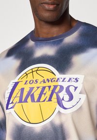 Kortærmet t-shirt med rund hals, der har et grafisk tryk af "Los Angeles Lakers" i lilla, gul og hvid på en blå tie-dye baggrund.