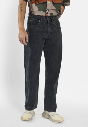 Black denim jeans with a straight fit, faded texture, five-pocket design, light stitching, and a high waist, paired with beige sneakers.