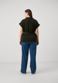 Quiltuotas tamsiai žalias viršus su trumpomis rankovėmis ir diržu juosmens srityje, derinamas su plačiomis mėlynomis džinsomis. Tinklinė medžiaga, laisvas siluetas.