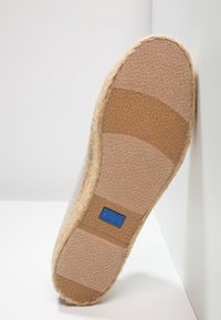 Semelle d'une espadrille beige avec un grip en caoutchouc texturé et une étiquette bleue "keds" près du centre.