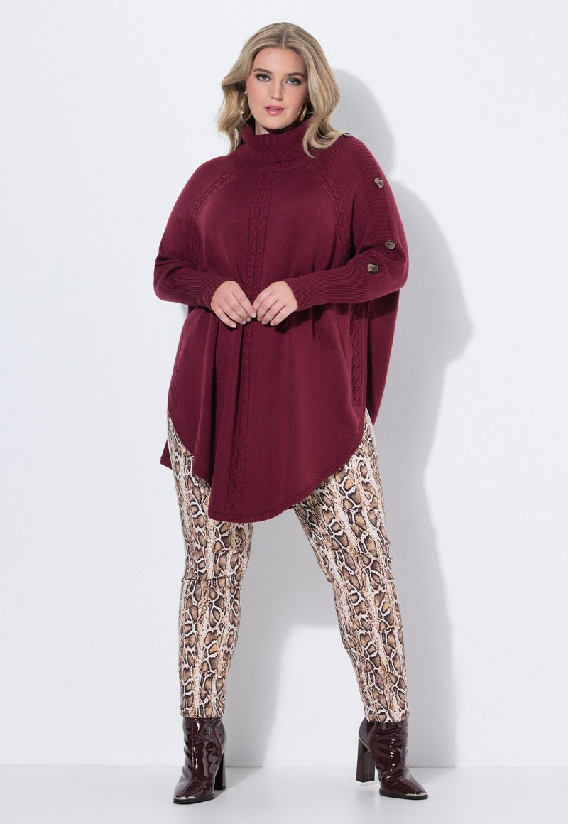 Pull en tricot bordeaux avec un col haut et des détails de boutons, associé à un pantalon à motif serpent et des bottes à talons noires brillantes.