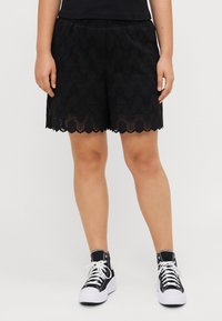 Shorts neri in pizzo con orlo a scallop, motivo dettagliato e vita elastica, abbinati a sneakers alte nere.
