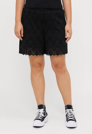 Schwarze Spitzen-Shorts mit gewelltem Saum, detailliertem Muster und elastischem Bund, kombiniert mit schwarzen High-Top-Sneakern.