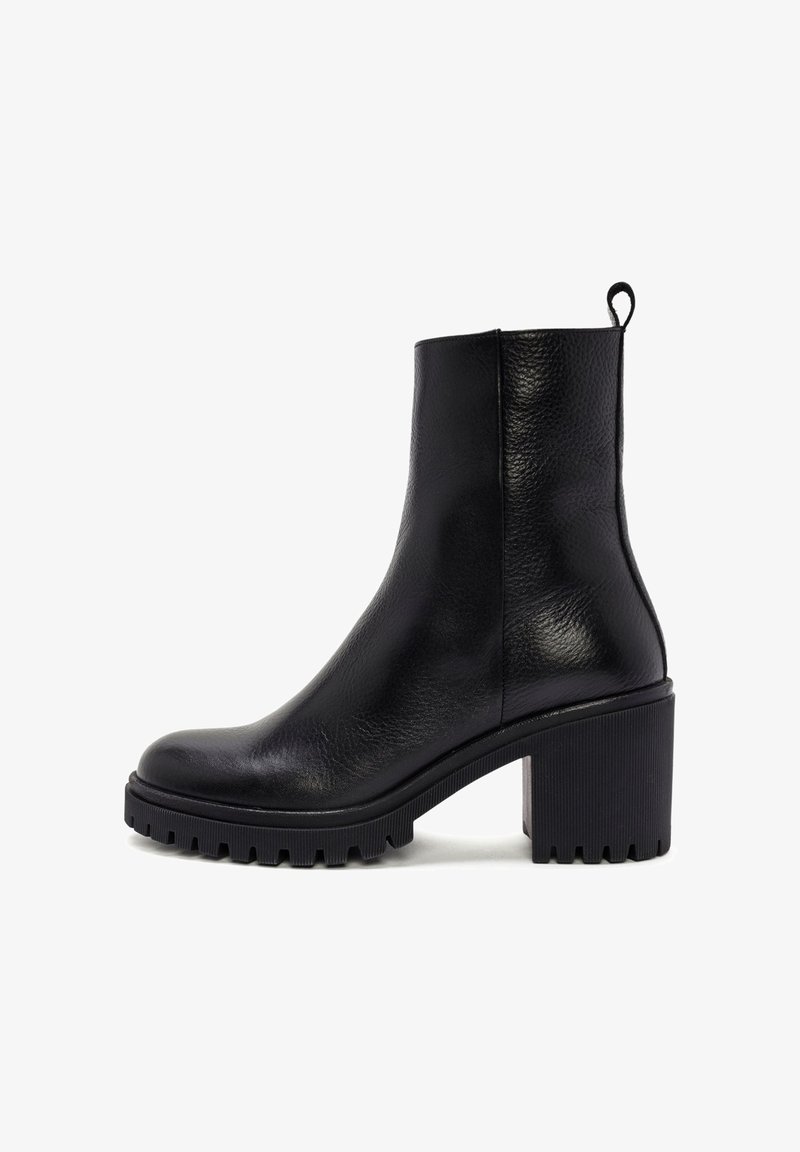 Bottines plates en cuir noir avec un bout rond, finitions texturées et un talon épais. Elles possèdent une tirette à l'arrière et une semelle rainurée.