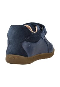Zapato de cuero y ante azul marino con acabado texturizado, que cuenta con una correa de Velcro, talón reforzado y suela de goma marrón con la marca "GEOX".