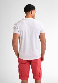 Camiseta de algodón blanca de manga corta, combinada con pantalones cortos cargo rojos a la altura de la rodilla, que presentan bolsillos laterales y un corte relajado.
