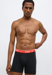 Fekete férfi boxeralsó piros Nike logóval díszített derékrésszel, testhezálló szabással és sima anyagból. A design egyszerű és praktikus.