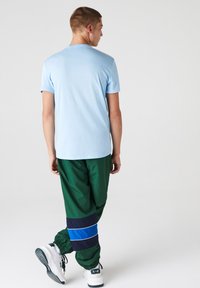 Camiseta de algodón azul claro y pantalones de chándal verde oscuro con rayas horizontales azules y marinas, con puños elásticos y zapatillas blancas.