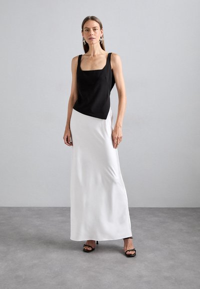 Black sleeveless top with square neckline paired with a white floor-length skirt. Smooth fabric and subtle drape, with strappy black heels.