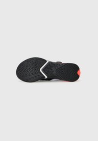 Suola di scarpa sportiva nera con motivo a zigzag, caratterizzata da un design testurizzato e una spruzzata di arancione brillante sul tallone.