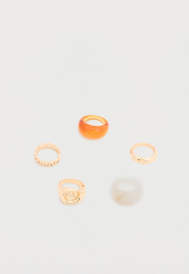 Cinq bagues assorties comprenant une bande orange translucide, une bande en or avec une spirale, une bande en or texturée, une bande en or lisse et une bande beige translucide.