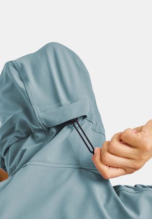 Hand, die schwarzen Kordelzug an hellblauer Kapuzenjacke von hinten vor einfachem Hintergrund anpasst.