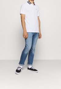 Bílé polo tričko s límcem v námořnické modré a červené pruhy, světle modré zúžené džíny a černé tenisky s bílou podrážkou a tkaničkami.