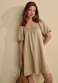 Kurzärmeliges Kleid mit quadratischem Ausschnitt aus einem hellbeigen, strukturierten Stoff. Es verfügt über geraffte Puffärmel, eine lockere Passform und einen knielangen Saum.