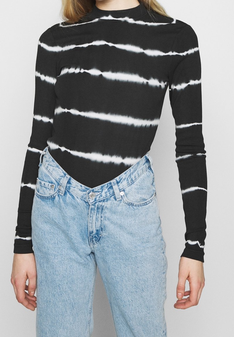 Czarny top z długim rękawem w białe paski typu tie-dye, zestawiony z jasnoniebieskimi, wysokim stanem jeansami, posiadającymi zapięcie na guziki i boczne kieszenie.