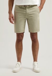 Khaki lühikesed püksid tekstuuriga viimistlusega, elastse vöökoha ja küljetaskutega, koos valgete tossudega. Neutraalne värvipalett.