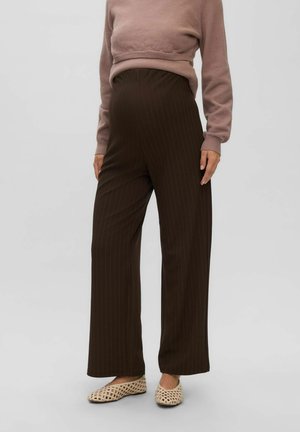 Personne portant un pantalon marron à larges jambes à rayures taille haute, un pull court mauve et des chaussures tissées beiges à enfiler sur fond gris.