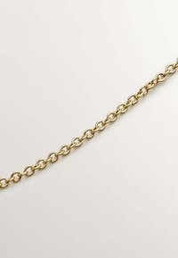 Cadena de metal dorado con eslabones ovalados, textura suave y acabado pulido, dispuesta en diagonal sobre un fondo claro.