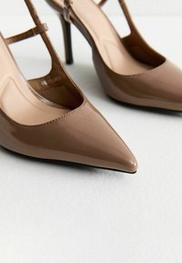 Zapatos de tacón alto de charol marrón con diseño de punta afilada, con tiras finas alrededor del tobillo y un acabado liso y brillante.