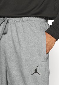 Šedé flísové tepláky s elastickým pasem a stahovací šňůrou, s černým logem Jumpman na levém stehně.