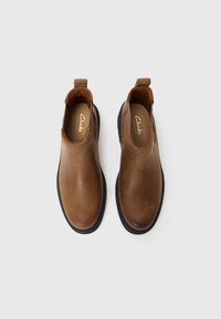Braune Lederstiefeletten mit glatter Textur, runder Spitze, elastischen Seiteneinsätzen und einer robusten schwarzen Gummisohle. Markenlogo ist im Inneren sichtbar.