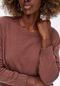 Brązowy, dziany sweter z prążkowanym okrągłym dekoltem i fitted mankietami. Tkanina ma miękką teksturę, wykazując subtelny połysk.