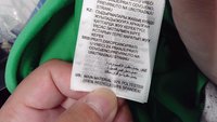 Zeleni odjevni etiketa s uputama za njegu i detaljima o materijalu: 92% poliester (100% recikliran) i 8% spandeks, s tekstom na više jezika.
