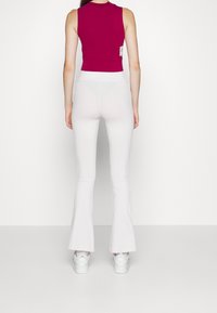 Hedvábný, bezrukávový magentový crop top spárovaný s bílými rozšířenými legínami. Model nosí bílé tenisky. Jednoduchý design s hladkou texturou.