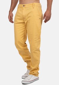 Pantaloni gialli in cotone con taglio dritto, dotati di passanti per cintura e dettagli di cucitura sottili, abbinati a sneaker bianche basse.