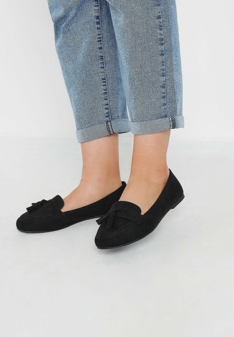 Svarta mockaloafers med en bård detalj på framsidan, platt sula och mjuk yta, tillsammans med uppvikta ljusa denimjeans.