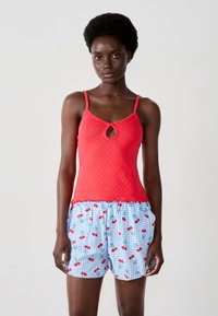 Top rosso senza maniche con dettaglio a chiave, abbinato a pantaloni corti in gingham blu con motivo a ciliegia. Tessuto liscio e cintura elastica.
