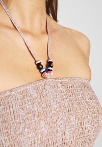 Pärlarmband med ett mönstrat snöre; innehåller flerfärgade p ärlor, inklusive svart, vitt, blått och blommönster, på en strukturerad beige topp.