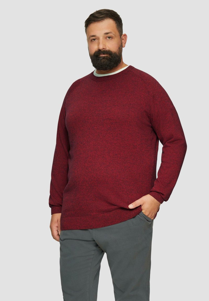 Bordeaux gebreide trui met een ronde hals, lange mouwen en geribbelde manchetten, gecombineerd met grijze broek. Zachte textuur met een subtiel patroon.