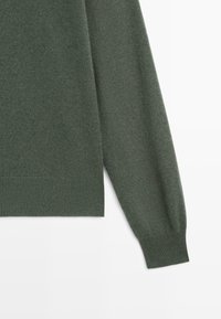 Mörkgrön stickad tröja med långärmade ärmar, ribbade muddar och en slät textur. Tyget verkar mjukt och lätt.