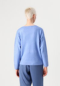 Sweatshirt en tricot bleu au toucher doux, avec des manches raglan et un large col. Poignets et ourlet côtelés, porté par-dessus un pantalon bleu.