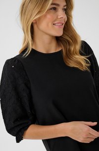 Svart t-shirt med texturerade svarta puffärmar med blommönster. Enkel, figursydd design med rund halsringning.