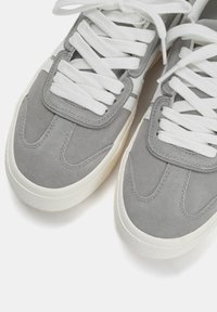 Baskets en suède gris avec des lacets et des détails blancs. Équipées d'une languette rembourrée et d'une semelle texturée. Bout arrondi avec un design cousu.