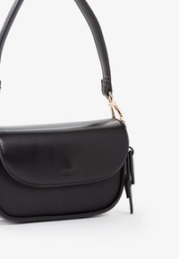 Borsa a spalla nera con pattina in pelle liscia, corpo strutturato, chiusura dorata e manico corto su sfondo bianco.