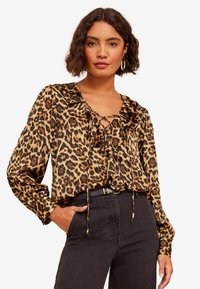 Halenka s leopardím potiskem, s волánkovým výstřihem, dlouhými rukávy a šněrováním, vyrobená z lehkého materiálu, kombinovaná s tmavými džínami s vysokým pasem.
