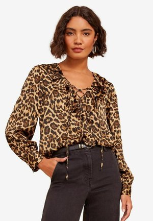 Halenka s leopardím potiskem, s волánkovým výstřihem, dlouhými rukávy a šněrováním, vyrobená z lehkého materiálu, kombinovaná s tmavými džínami s vysokým pasem.